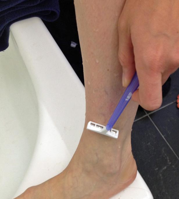 Eine Person rasiert sich mit einem blauen Einwegrasierer das Bein.