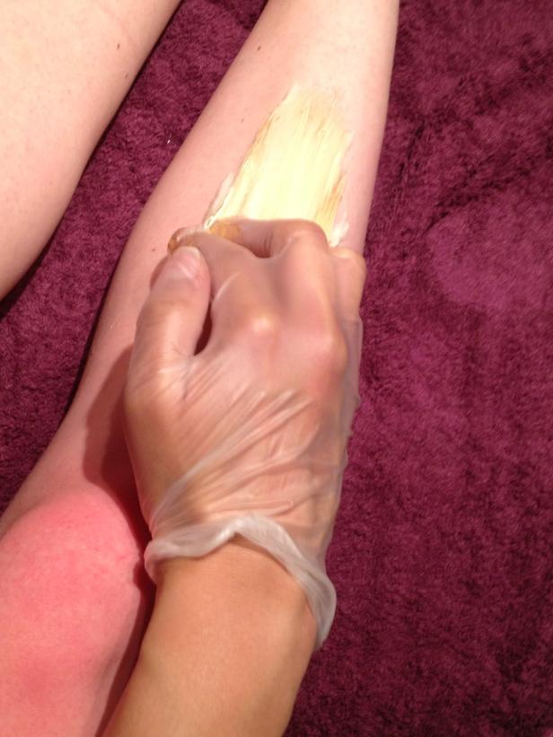 Eine Kosmetikerin trägt Wachs auf das Bein einer Kundin auf.