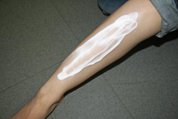 Eine Frau cremt ihr Bein mit einer weißen Lotion ein.