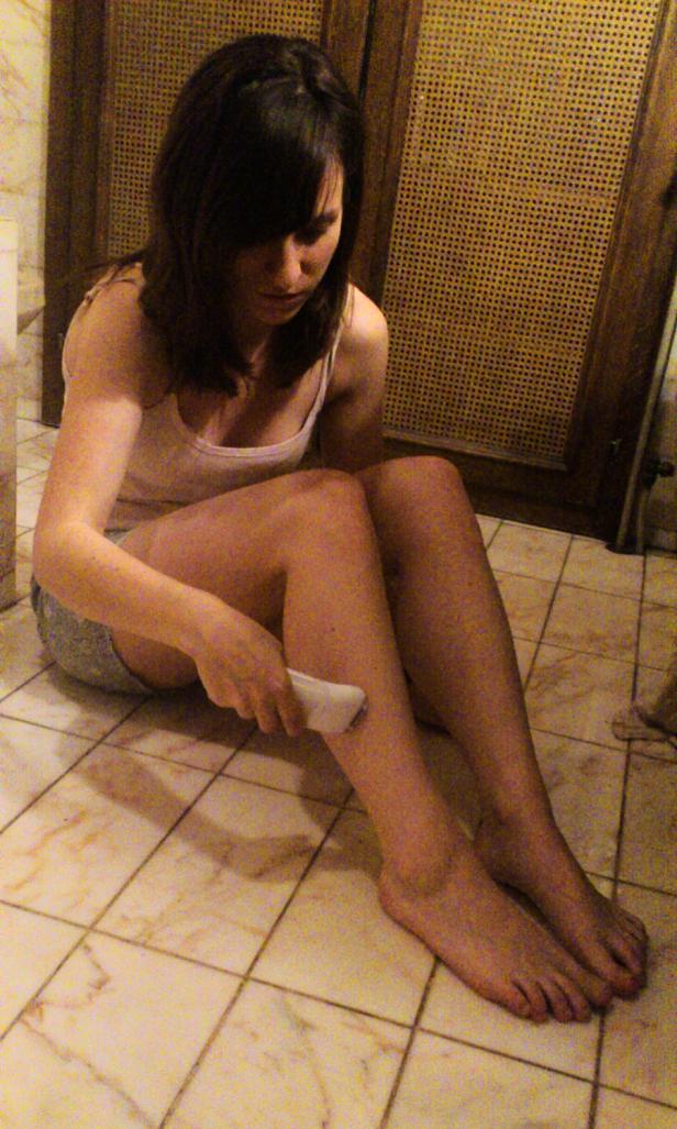 Eine Frau sitzt auf dem Badezimmerboden und epiliert ihre Beine.