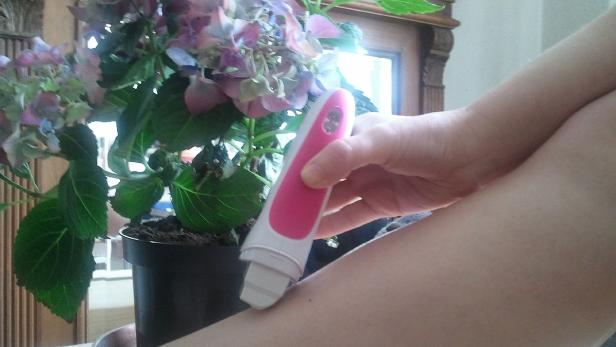 Eine Person benutzt ein Epiliergerät am Bein, im Hintergrund eine Hortensie.