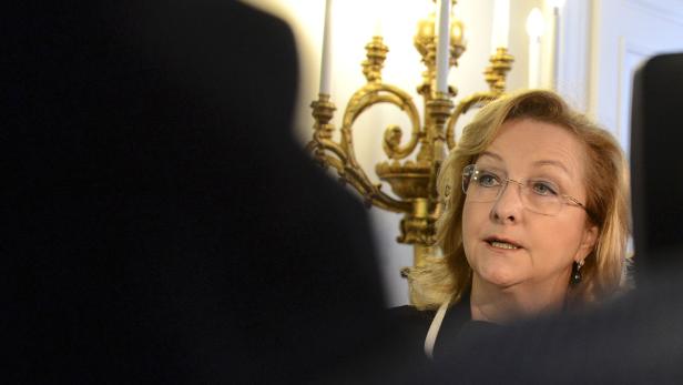 Eine Frau mit Brille spricht vor einem goldenen Kerzenständer.