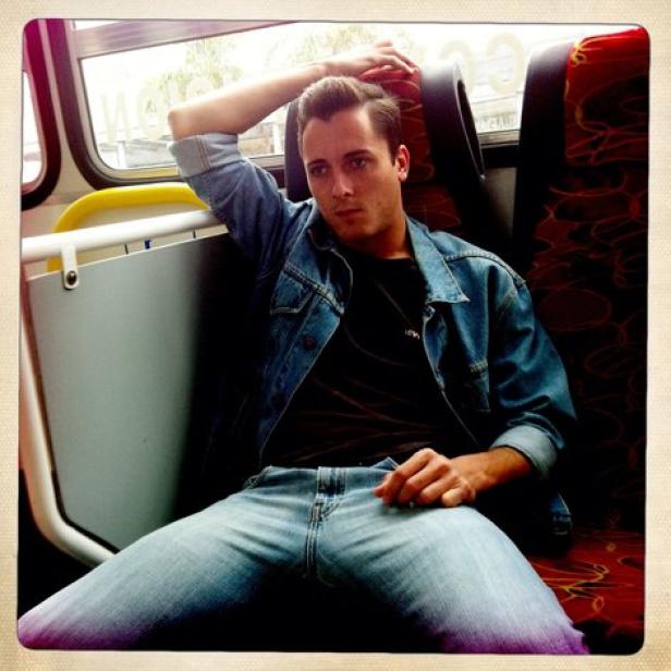 Ein Mann in Jeansjacke sitzt entspannt in einem Bus oder Zug.