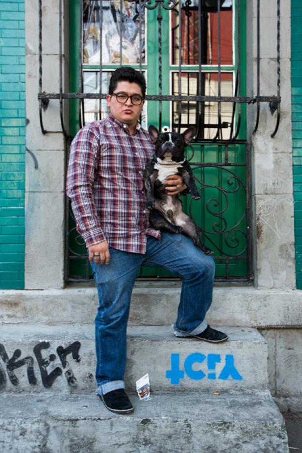 Ein Mann mit Brille hält eine Französische Bulldogge vor einer grünen Tür.