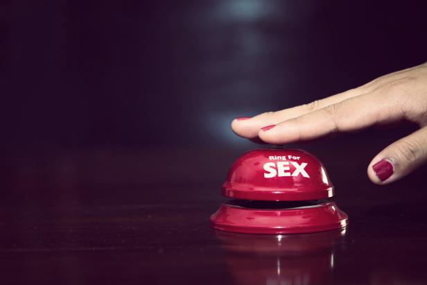 Eine Hand drückt einen roten Klingelknopf mit der Aufschrift „Ring For SEX“.