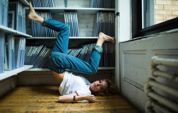 Eine Frau liegt auf dem Boden, die Füße an einem Bücherregal und einer Wand abgestützt.