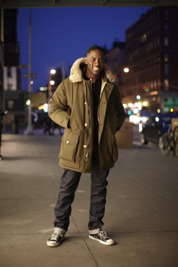 Ein Mann mit Winterjacke steht abends auf dem Bürgersteig.