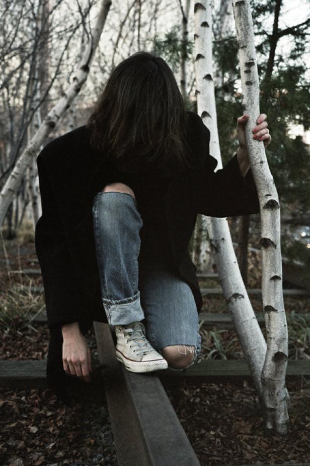 Eine Person mit zerrissenen Jeans posiert an einem Birkenstamm im Freien.