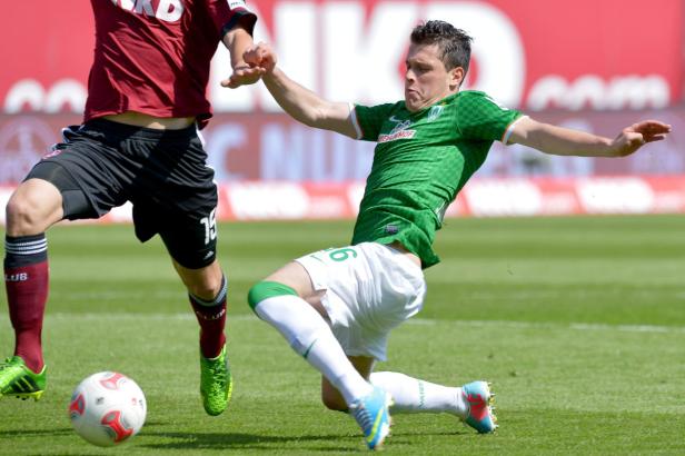 Ein Fußballspieler im grünen Trikot grätscht nach dem Ball.