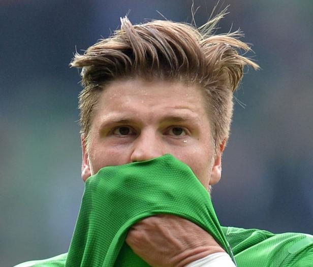 Ein Mann mit blonden Haaren hält ein grünes Trikot vor sein Gesicht.