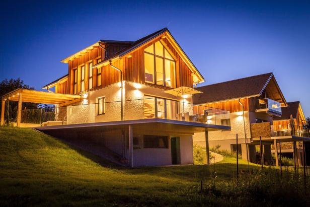 Moderne Holzhäuser mit Terrassen und abendlicher Beleuchtung.