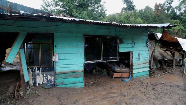 Ein beschädigtes, blaues Holzhaus ist von Schlamm bedeckt.
