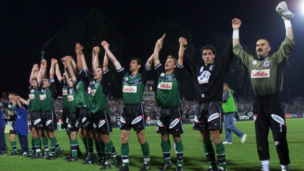 Eine Fußballmannschaft jubelt mit erhobenen Armen auf dem Rasen.