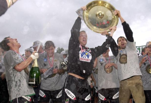 Fußballspieler feiern einen Sieg mit Champagner und der Meisterschale.