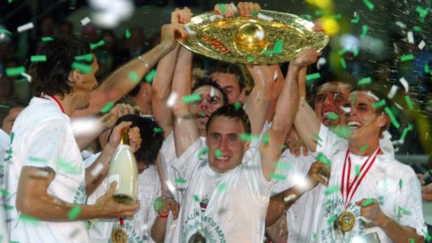 Eine Gruppe von Fußballspielern feiert mit einer Trophäe und Konfetti ihren Sieg.