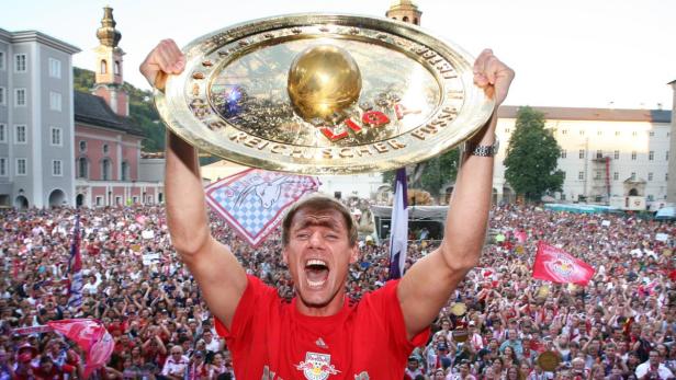 Ein Mann jubelt mit der Meisterschale der österreichischen Fußball Bundesliga in der Hand vor einer jubelnden Menschenmenge.