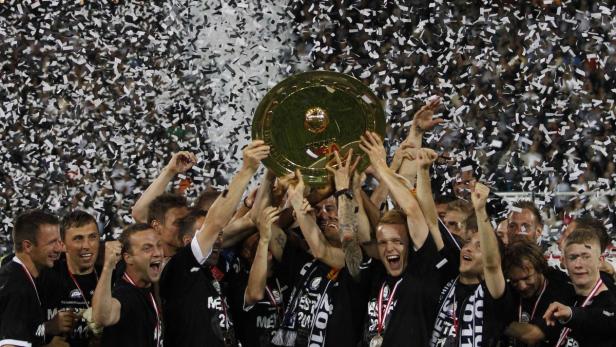 Eine Fußballmannschaft feiert mit der Meisterschale im Konfettiregen.