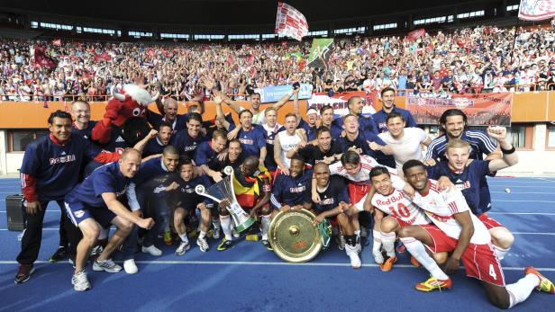 Die Fußballmannschaft feiert mit Fans und Pokal den Aufstieg.