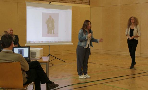 Eine Frau hält eine Präsentation vor einem Publikum in einer Turnhalle.