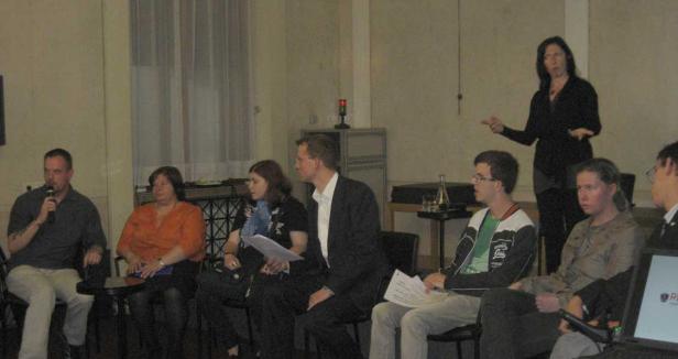 Eine Frau hält einen Vortrag vor einem sitzenden Publikum.