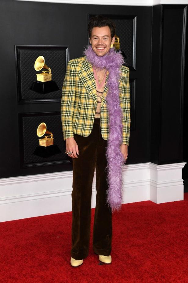 Harry Styles auf dem roten Teppich der Grammy Awards mit gelbem Blazer und lila Federboa.