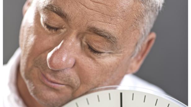 Ein Mann schläft mit dem Kopf auf einer Uhr.