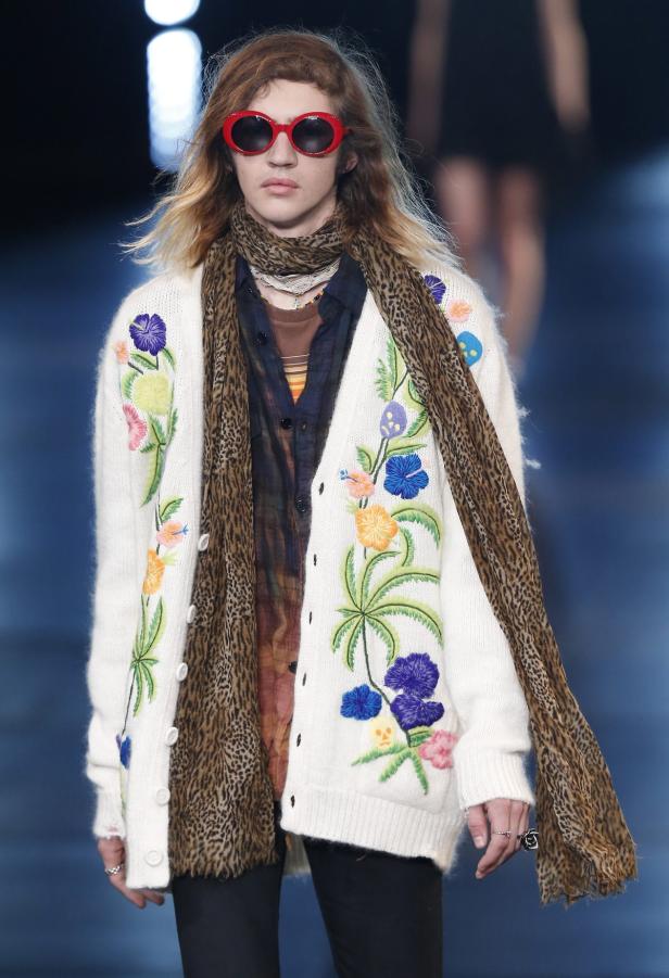 Ein Mann mit roter Sonnenbrille und einem bestickten Cardigan mit Leopardenmuster-Schal.