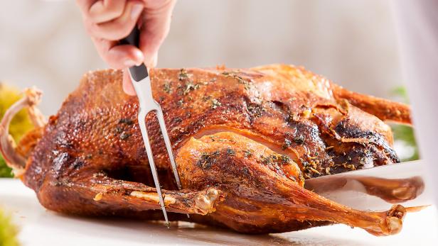 Ein Koch tranchiert eine gebratene Gans mit einer Tranchiergabel und einem Messer.