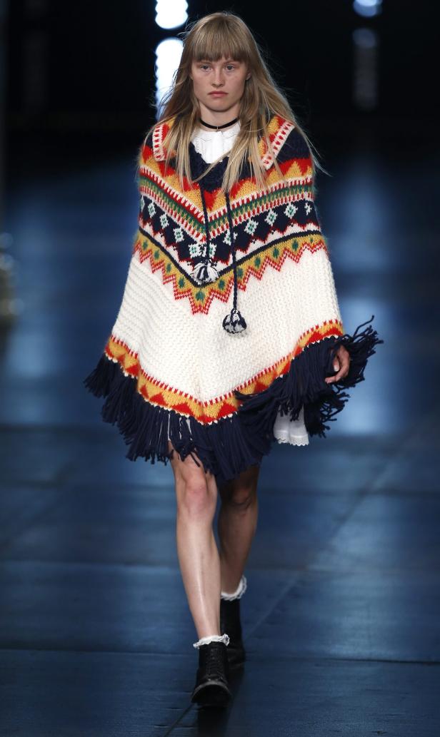 Ein Model trägt einen bunten Poncho mit Fransen auf dem Laufsteg.