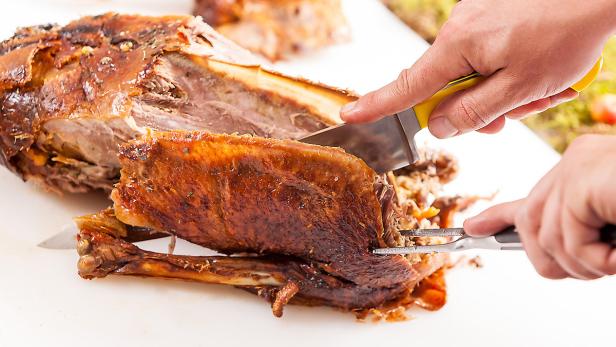 Ein Braten wird mit Messer und Gabel tranchiert.