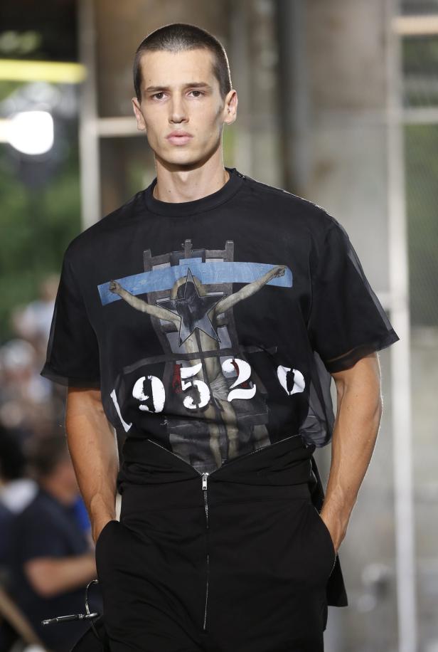 Ein Mann trägt ein schwarzes T-Shirt mit einem Aufdruck von 1952 und einem Kreuz.