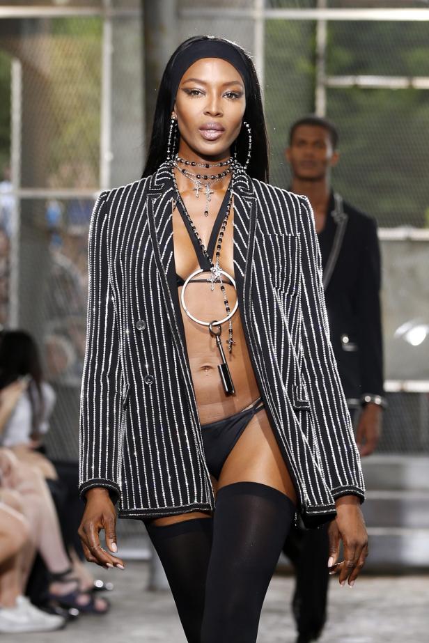 Naomi Campbell in einem gestreiften Blazer und schwarzen Accessoires auf einem Laufsteg.