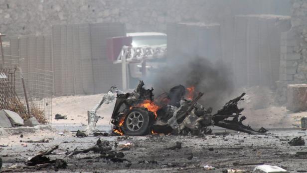 Ein ausgebranntes Autowrack raucht inmitten von Trümmern.