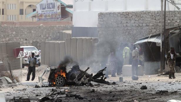 Ein ausgebranntes Auto raucht inmitten von Trümmern auf einer Straße.