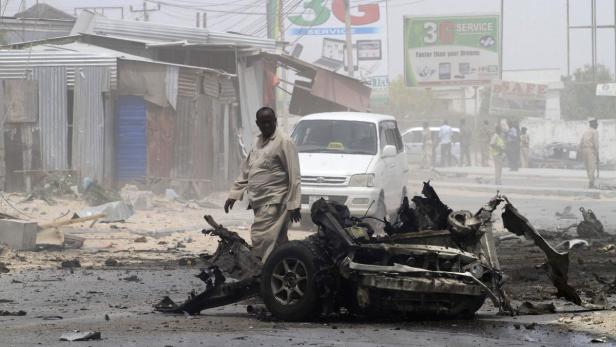 Ein Mann geht an einem zerstörten Auto vorbei; im Hintergrund ein Taxi und beschädigte Gebäude.