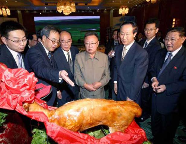 Kim Jong-il und andere Männer bei der Präsentation eines Spanferkels.