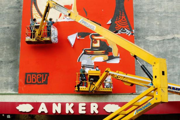 Zwei Arbeiter entfernen ein Wandgemälde von Shepard Fairey (OBEY) mit Hubsteigern der Firma Prangl.