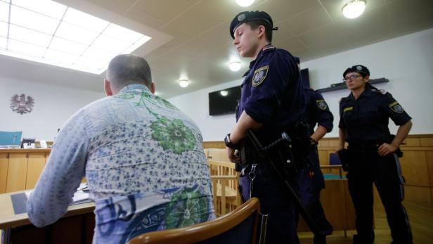 Ein Mann sitzt vor Gericht, bewacht von österreichischen Polizisten.