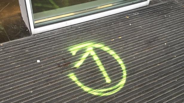 Ein grünes Graffiti-Symbol auf einer Fußmatte vor einer Tür.