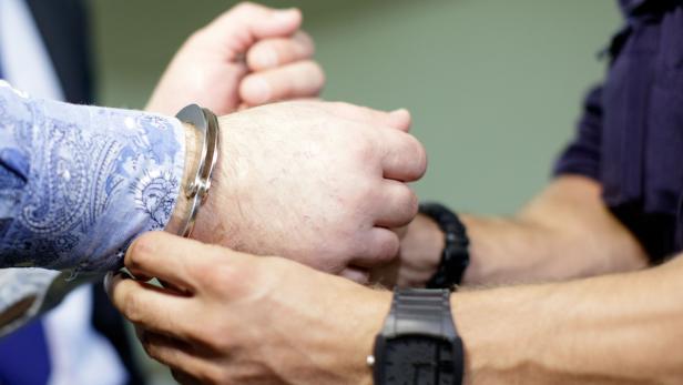 Ein Mann wird von einem Polizisten mit Handschellen gefesselt.