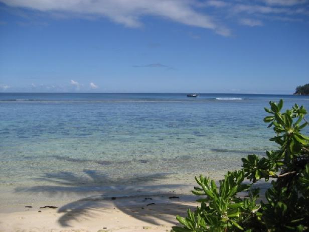 Ein ruhiger Strand mit türkisfarbenem Wasser und einem kleinen Boot am Horizont.