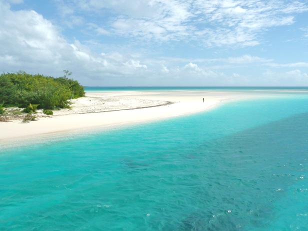 Ein tropischer Strand mit türkisfarbenem Wasser und einer einzelnen Person in der Ferne.