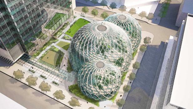 Drei miteinander verbundene Glaskuppeln, umgeben von Grünflächen und Gebäuden.