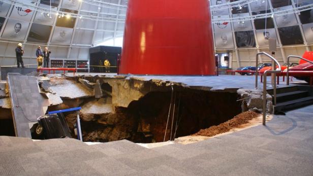 Ein großes Loch im Boden eines Museums, in dem ein Auto teilweise versunken ist.