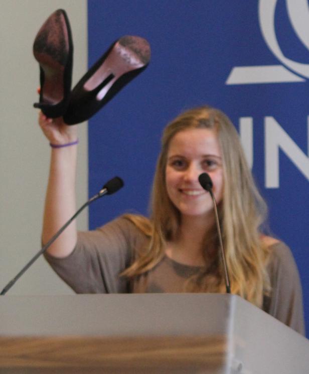 Eine junge Frau hält auf einem Podium ein Paar High Heels in die Höhe.