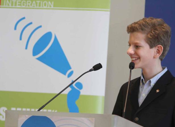 Ein junger Mann spricht lächelnd an einem Rednerpult mit Mikrofonen.