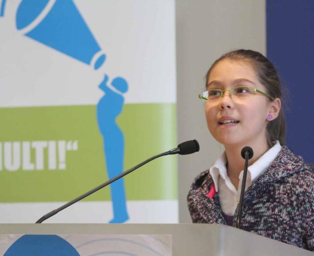 Ein junges Mädchen spricht bei einer Veranstaltung am Rednerpult.