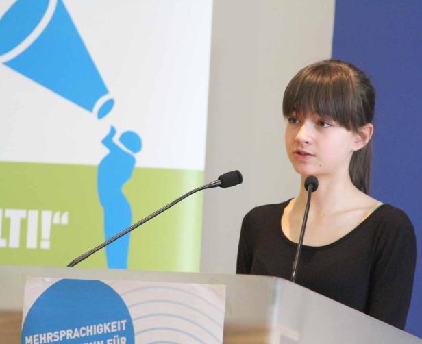 Ein junges Mädchen steht an einem Rednerpult und spricht in ein Mikrofon.