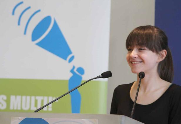 Eine junge Frau lächelt an einem Rednerpult mit Mikrofonen.