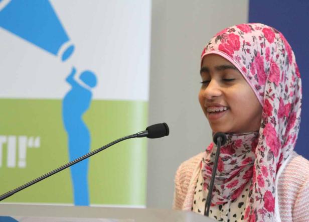 Ein junges Mädchen mit Kopftuch spricht am Rednerpult.